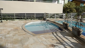 A swimming pool with a tiled deck, surrounded by potted plants and a metal railing. - Doce Lar de Bertioga (Bertioga)