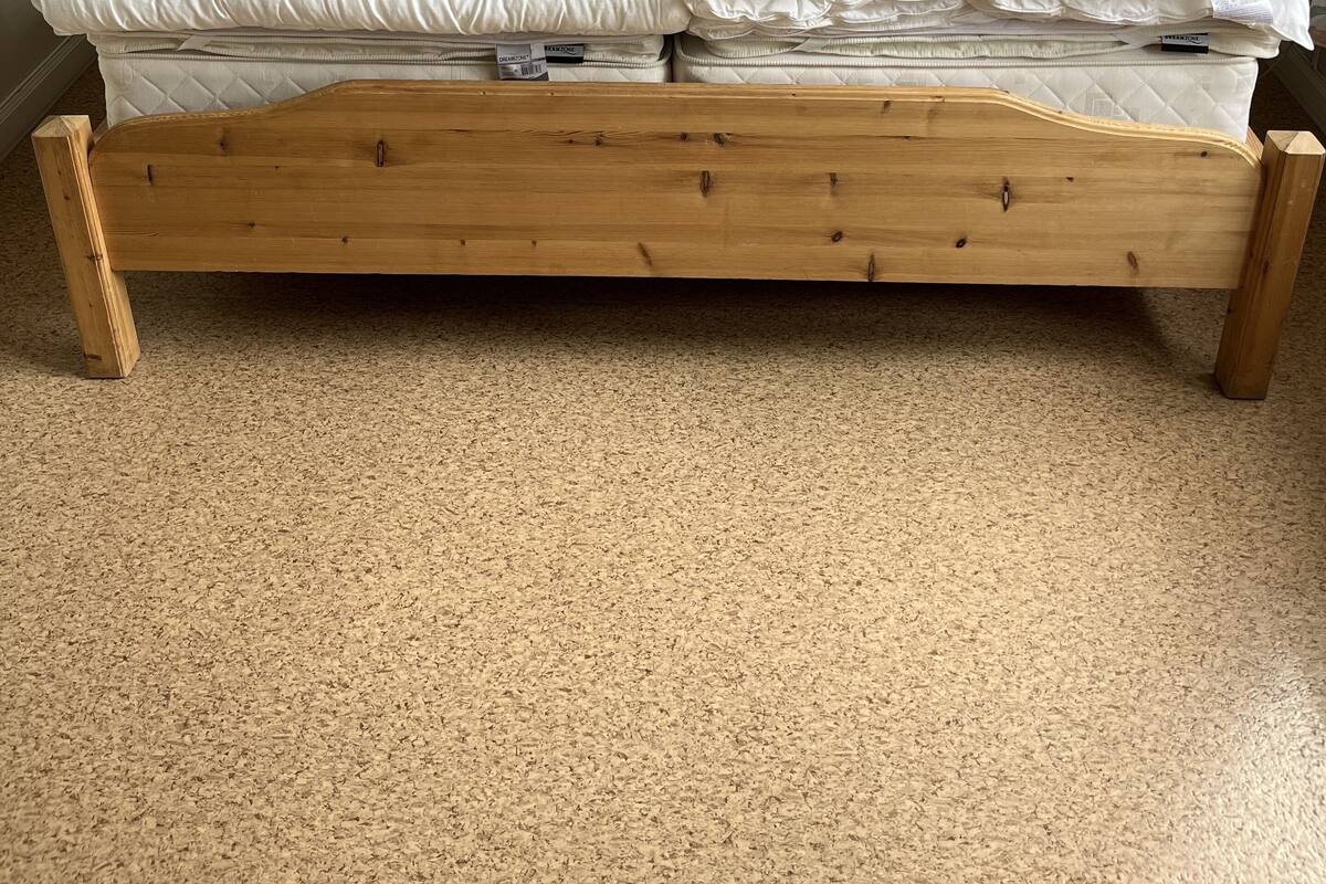 Una cama doble con estructura de madera, dos mesitas de noche y un cuadro colgado en la pared.