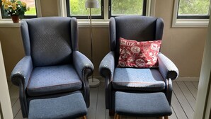 Two armchairs with matching patterns, a floor lamp, and a view of greenery through large windows.