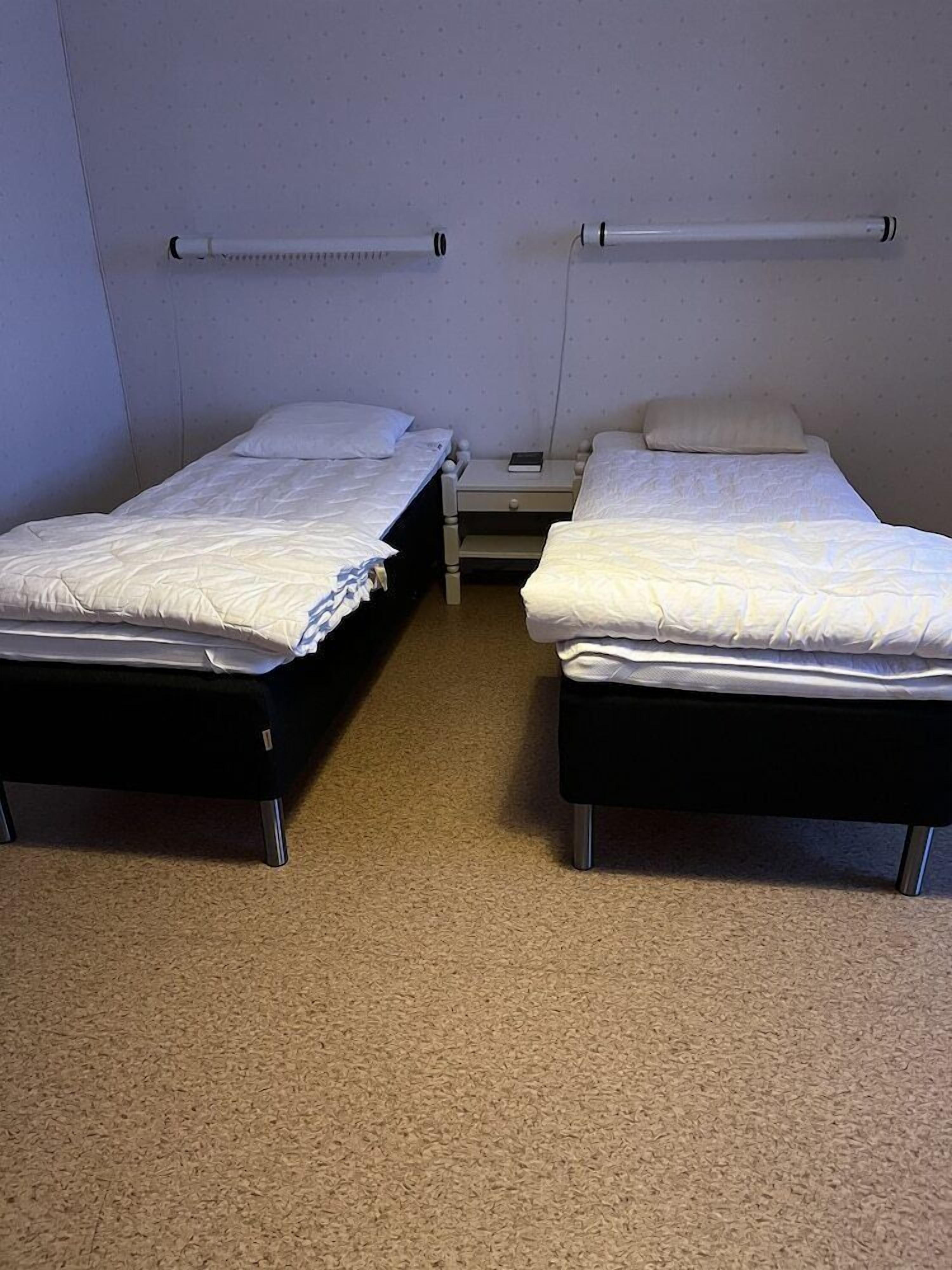 Two single beds with headboards, a small bedside table, and a wall-mounted shelf.
