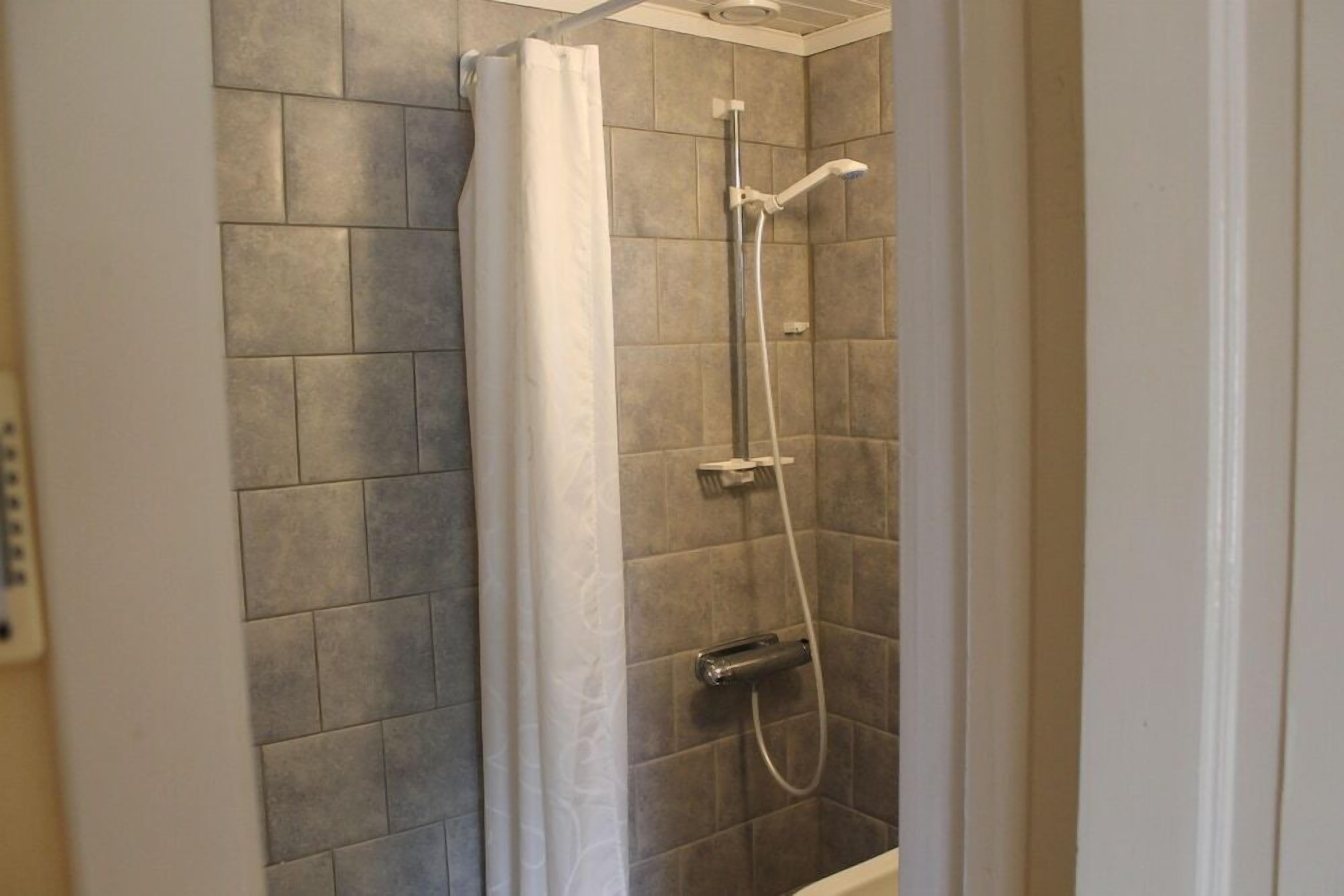 Ducha con cortina, cabezal de ducha de mano y panel de control en la pared.
