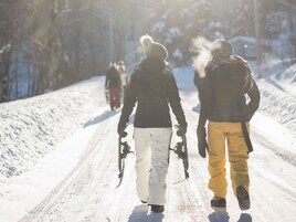 Carretera nevada con gente caminando, algunos llevando esquíes.