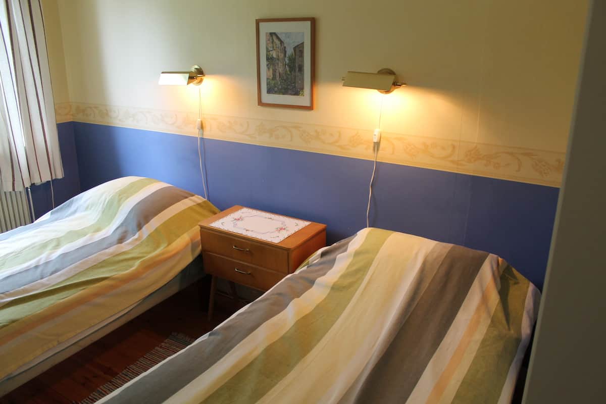 Una habitación con dos camas individuales, una mesita de noche con lámpara y un cuadro enmarcado en la pared.