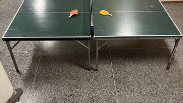 A ping pong table with two paddles in a room with a tiled floor and a yellow caution tape marking an area.