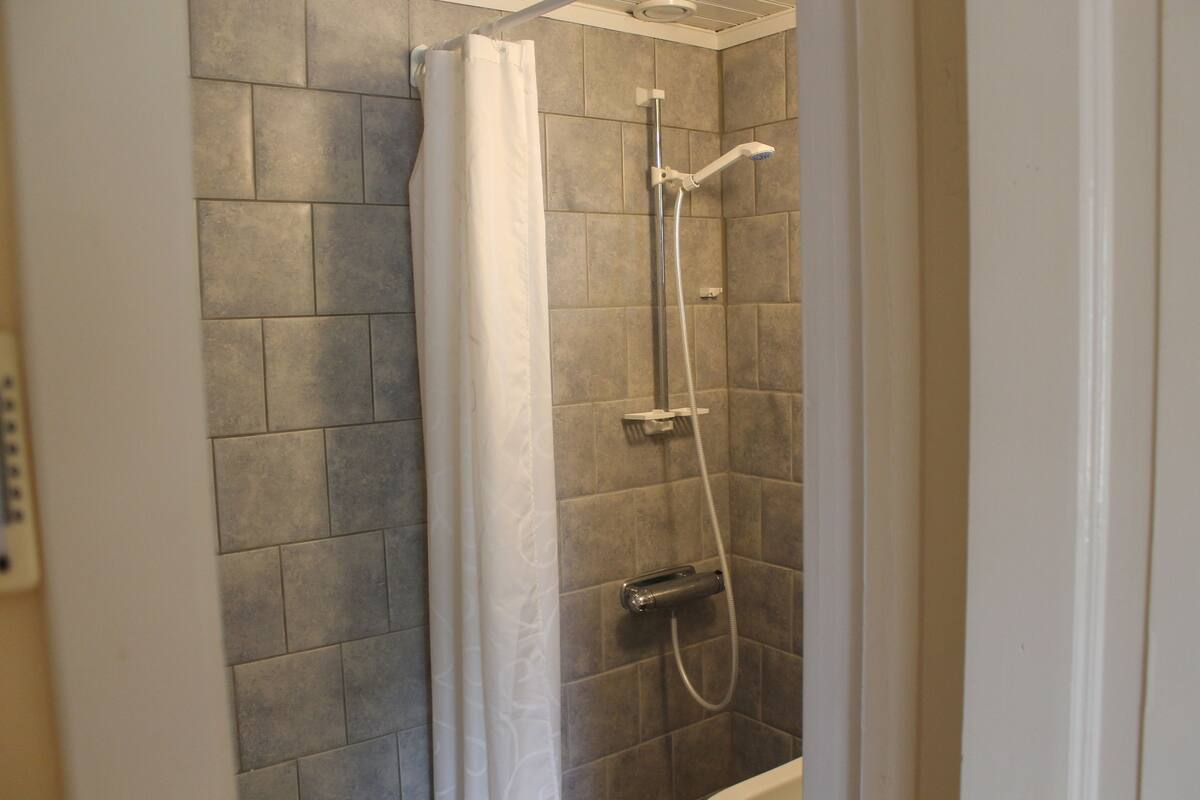 Una ducha con cabezal de ducha de mano y mandos en la pared.