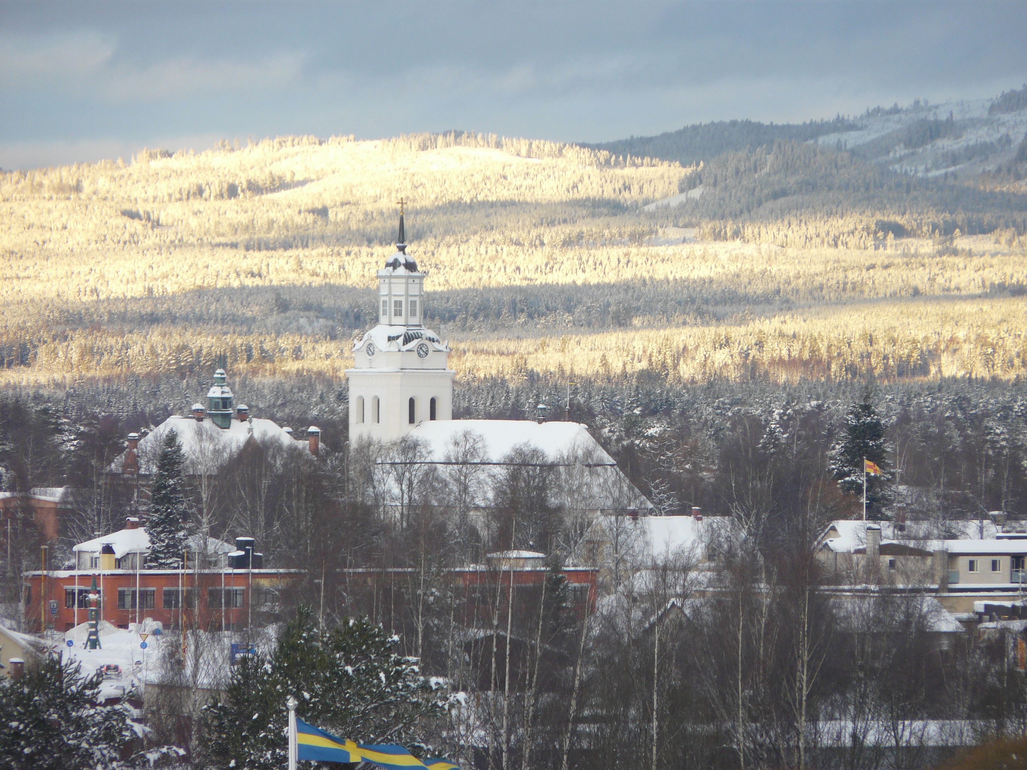 A church with a bell tower, surrounded by snow-covered buildings and trees.