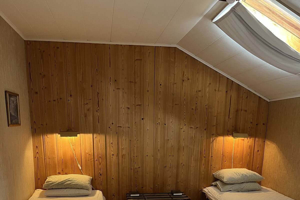 Una habitación con paredes de paneles de madera, dos camas con ropa blanca, un aparador y un ventilador de techo.