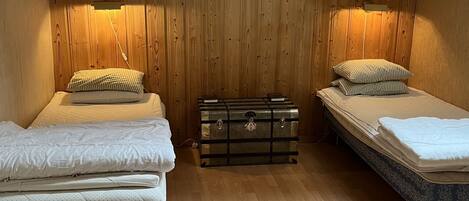 A room with wooden panel walls, two beds with white bedding, a chest of drawers, and a ceiling fan.