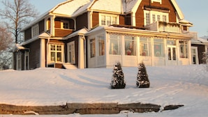 A large, two-story wooden house with a snow-covered roof and a balcony.