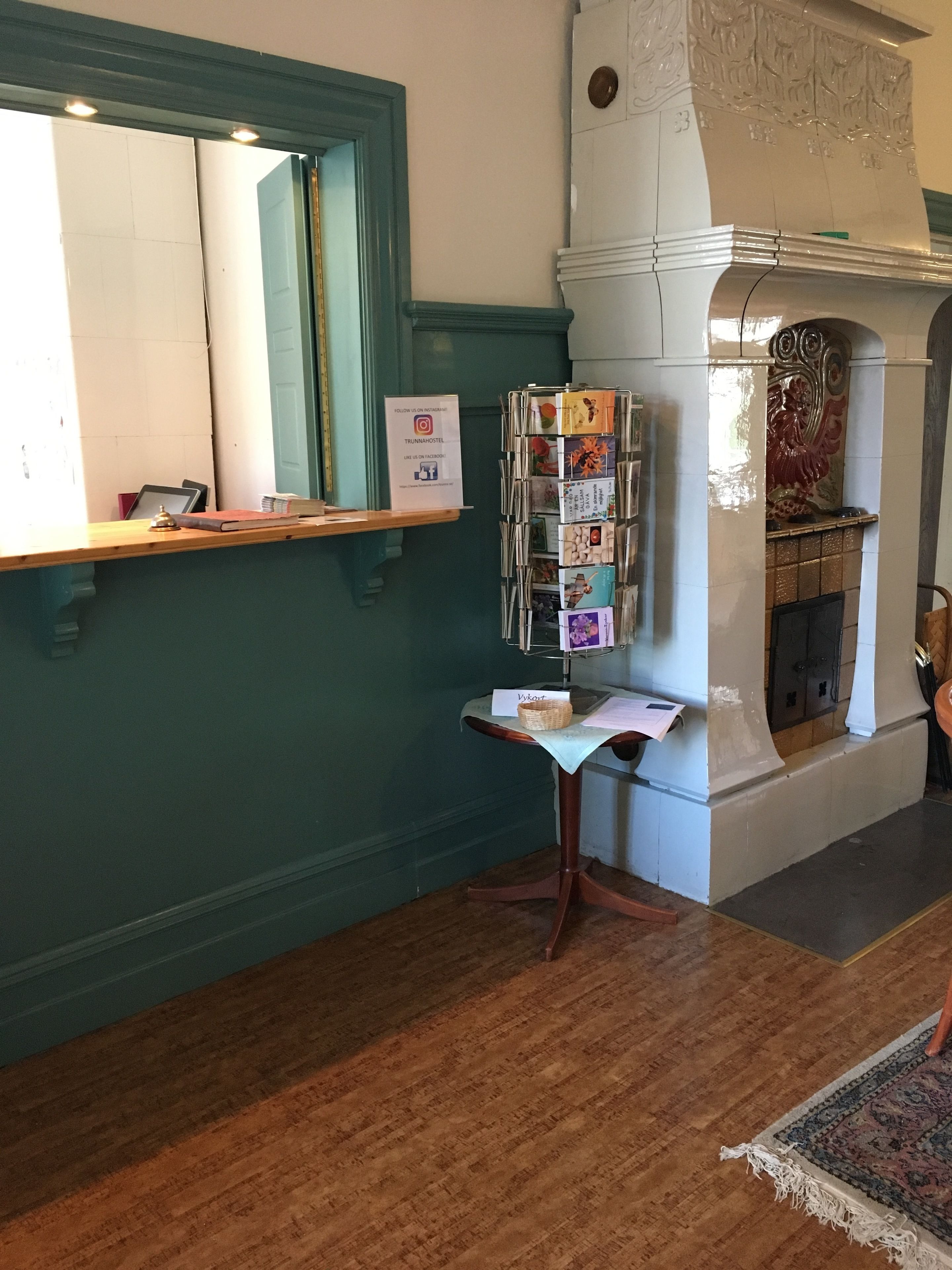 A reception area with a wooden desk, a mirror, a wall-mounted sign, a fireplace, and a magazine rack.