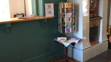 A reception area with a wooden desk, a mirror, a wall-mounted sign, a fireplace, and a magazine rack.