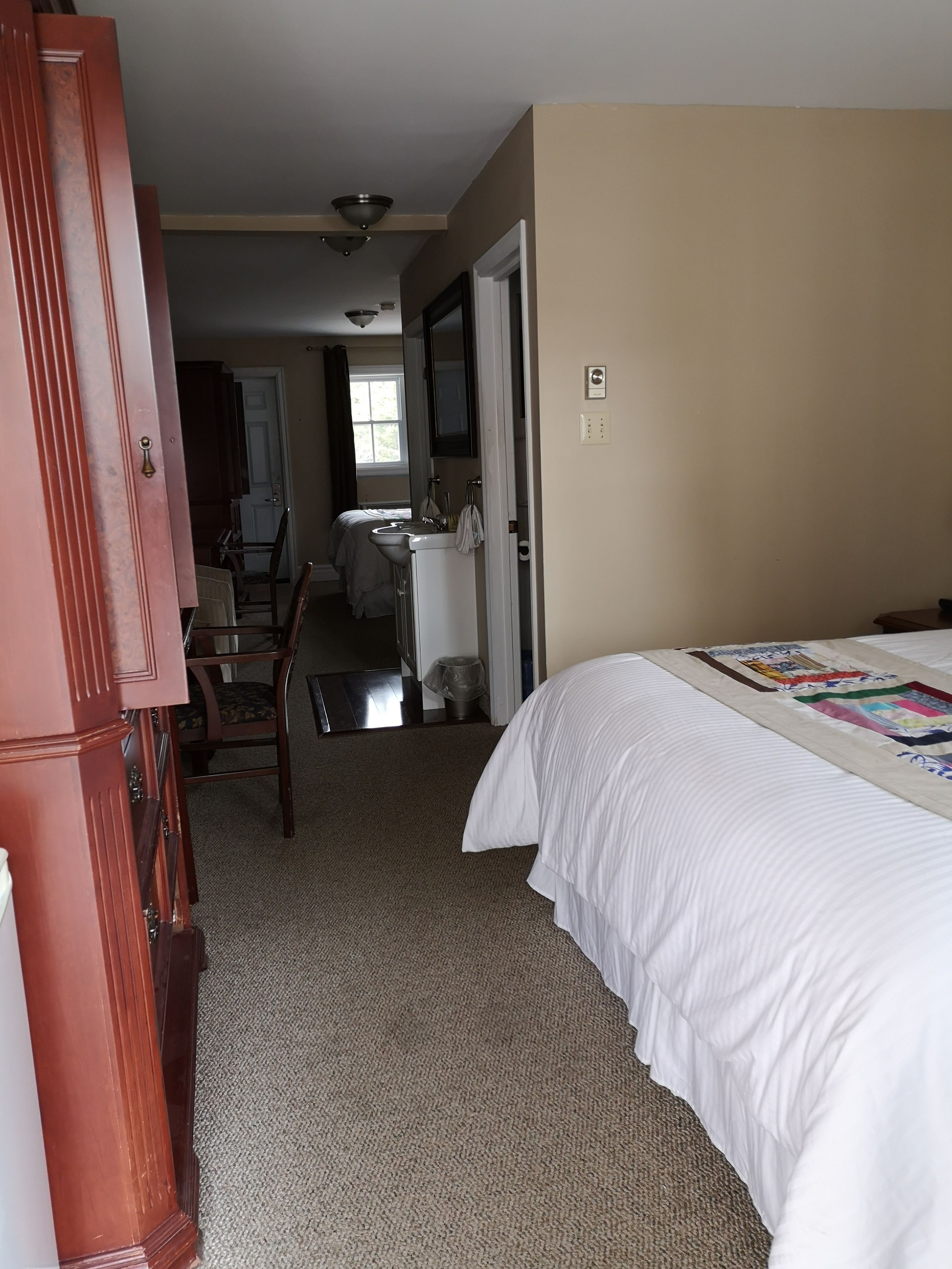 A bedroom with a bed, a desk, and a chair. There is a window with curtains, a door, and a mirror.