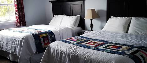 A hotel room with two beds, a window with curtains, a lamp, and a dark wooden headboard.