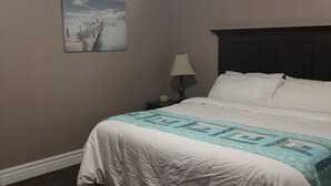 Un dormitorio con cama, mesita de noche, lámpara, aire acondicionado de pared y un cuadro de un muelle.