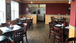 Interior de restaurante con paredes de paneles de madera, una barra central y varias mesas y sillas.