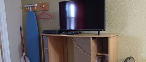 Een houten entertainmentskast met een flatscreen televisie, een bezem en een surfplank voor een gestructureerde muur.