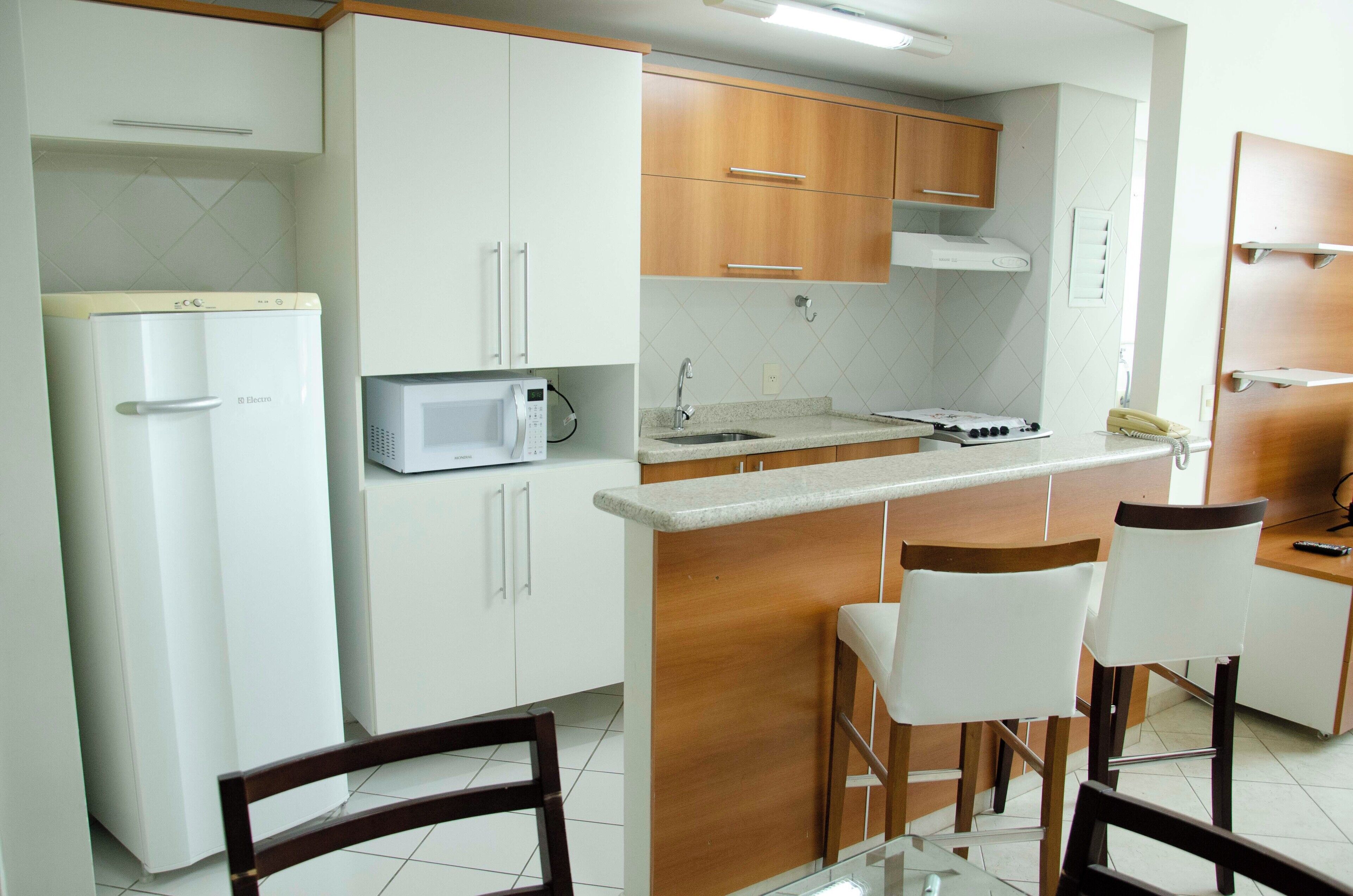 Cocina compacta con armarios blancos, microondas, estufa y dos taburetes de bar.