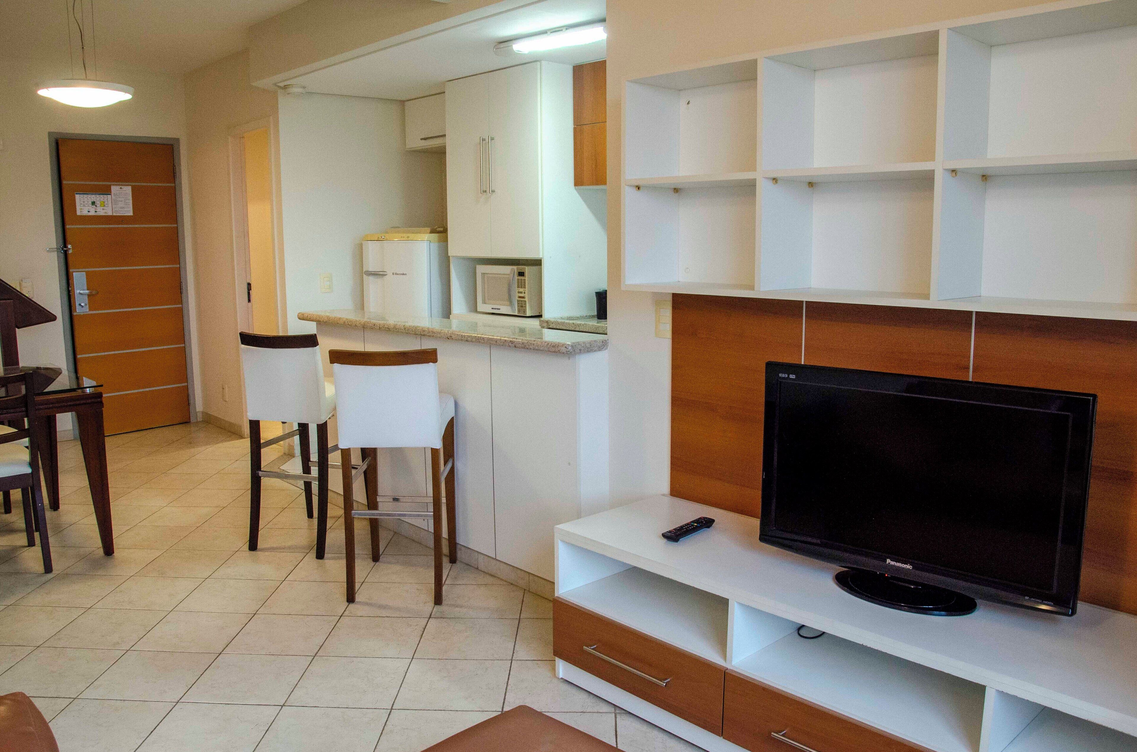 A compact living space with a kitchenette, a dining area, and a TV on a stand.