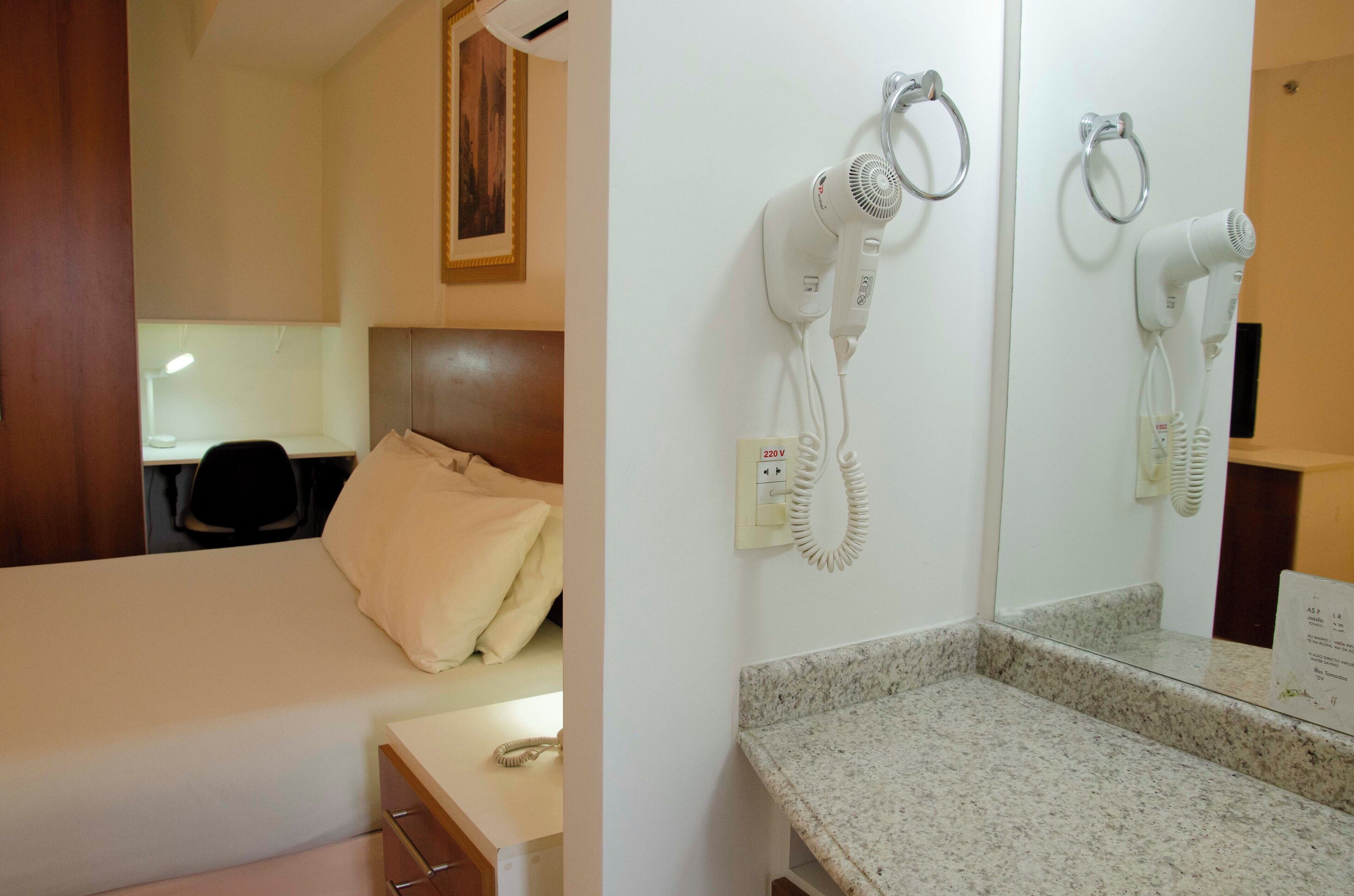 Habitación de hotel con cama, escritorio, silla y secador de pelo montado en la pared.