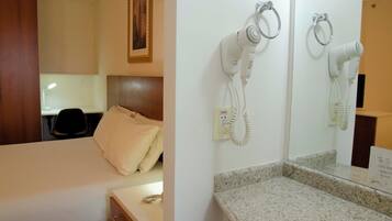 Habitación de hotel con cama, escritorio, silla y secador de pelo montado en la pared.
