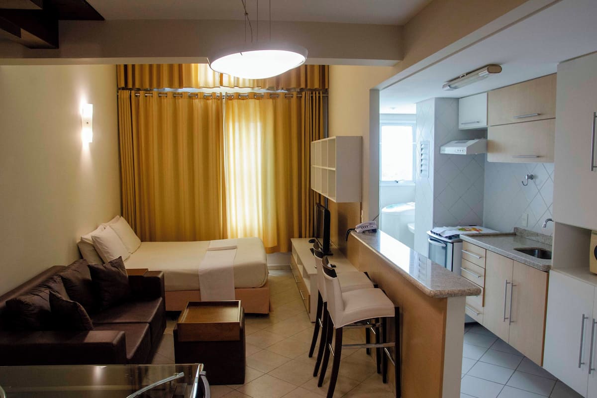 A modern hotel room with a bed, a sofa, a dining area, and a kitchenette.