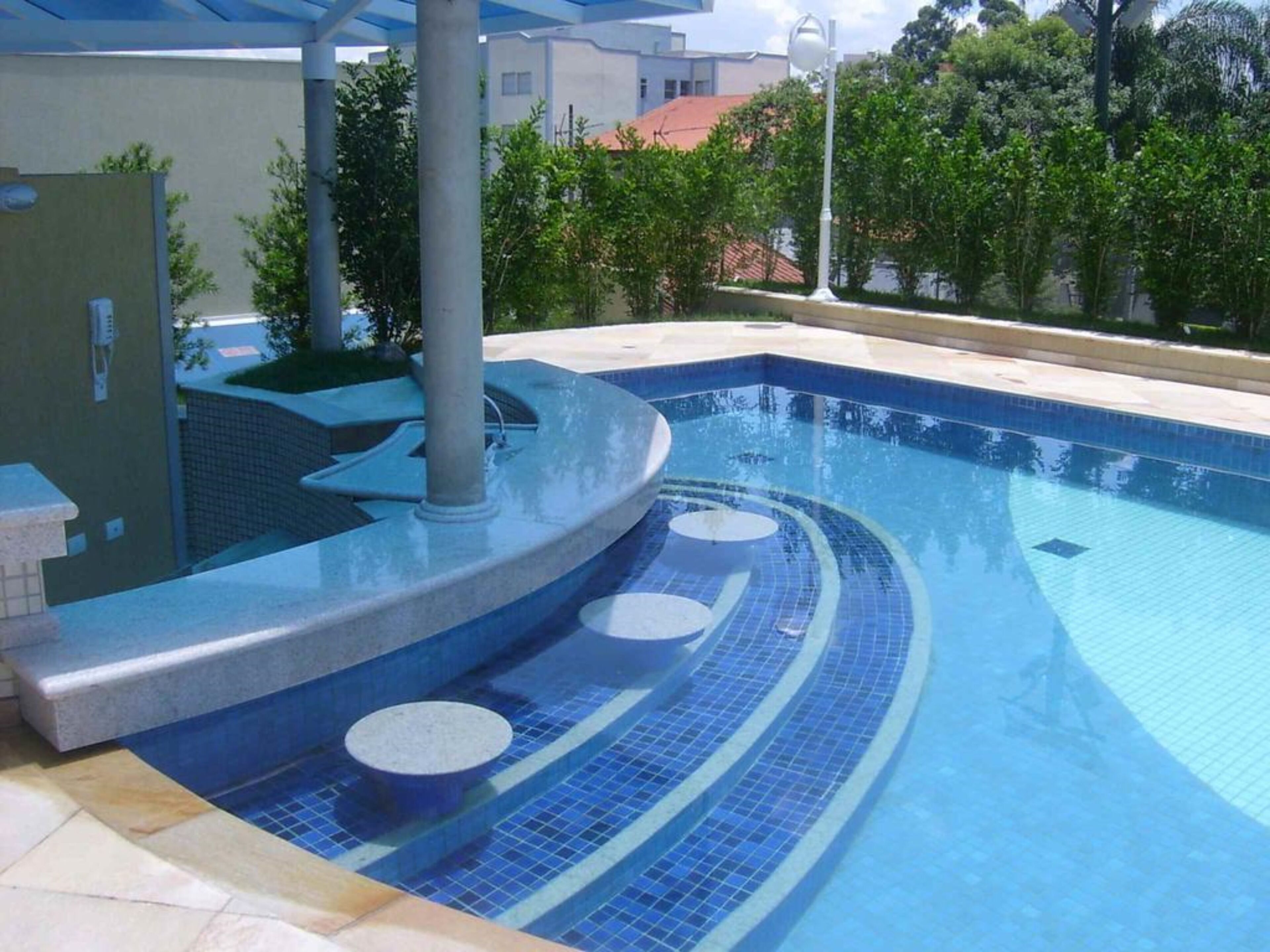 A swimming pool with a curved design, surrounded by a tiled deck and a small seating area.