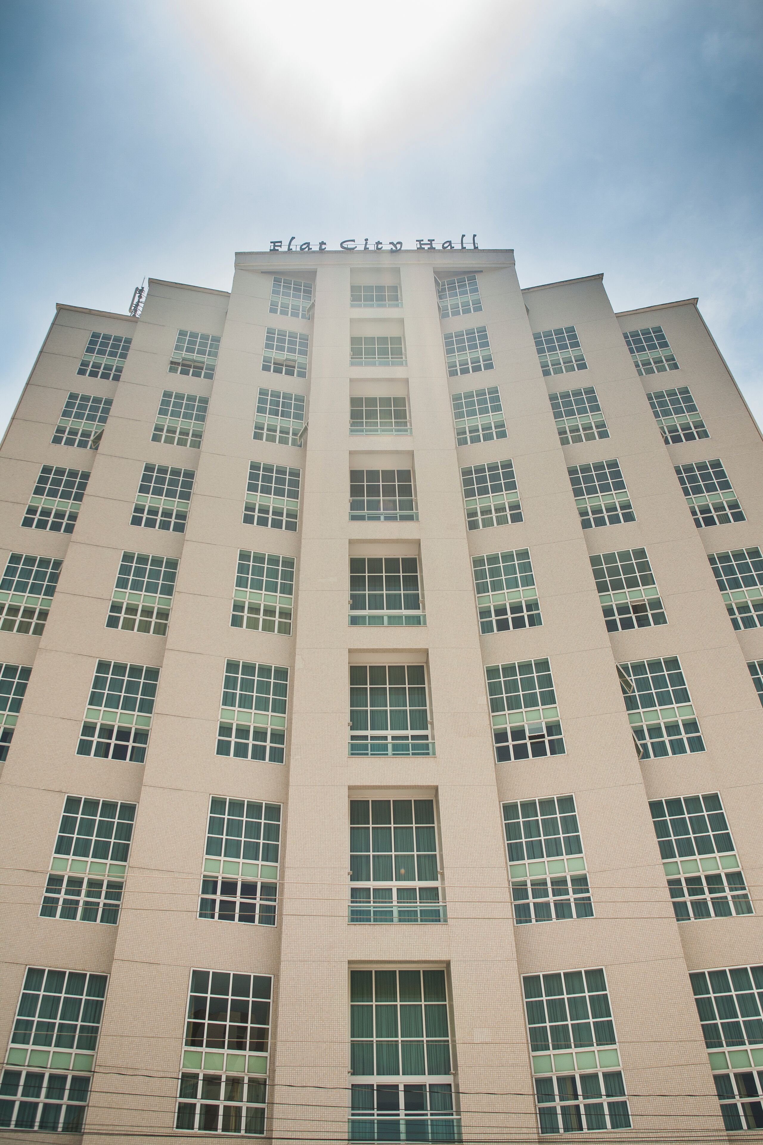 Um edifício alto e moderno com uma placa no topo que diz 'Flat City Hall'.