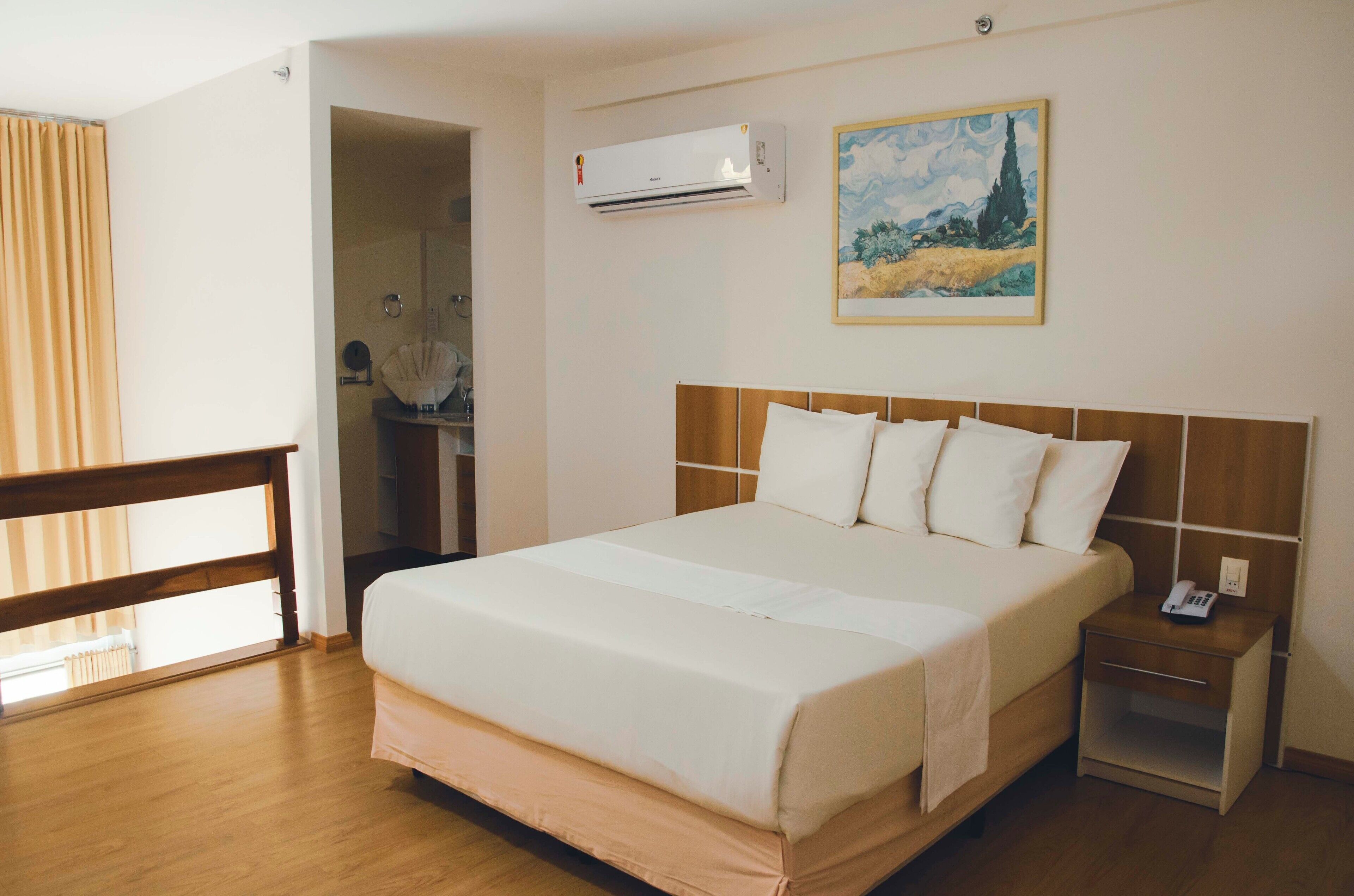 Une chambre d’hôtel avec un grand lit, une table de chevet, un appareil de climatisation, un tableau et une vue sur l’extérieur.
