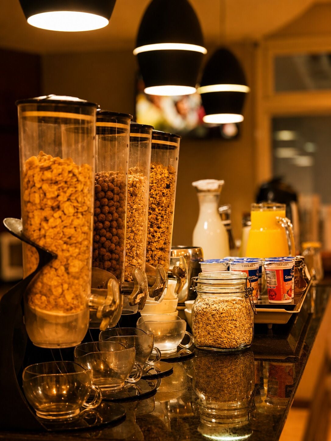 Una barra de desayuno con varios dispensadores de alimentos, incluyendo cereal y granola, además de un dispensador de jugo.