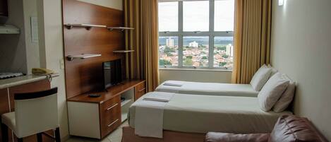 Habitación de hotel con cama, escritorio con televisor, una silla y vista a la ciudad desde la ventana.