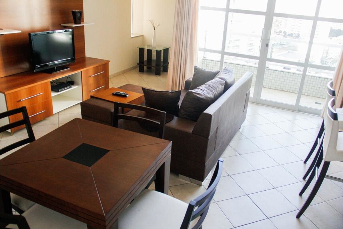 A modern living room with a sofa, a TV, a dining table, and a balcony with a view.