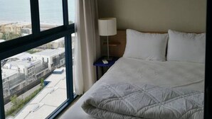 A hotel room with a large window offering a view of the city and the sea. - Baan Thew Talay Blue Sapphire 353 (Cha-am)