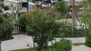 A modern high-rise building with multiple balconies and a well-maintained garden area with red flowers. - Baan Thew Talay Blue Sapphire 353 (Cha-am)