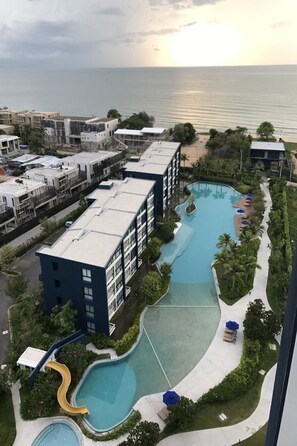 A resort with a large pool area, including a slide, surrounded by buildings and a view of the sea. - Baan Thew Talay Blue Sapphire 353 (Cha-am)