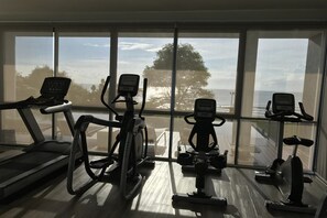 Ein Fitnessstudio mit Laufbändern, Crosstrainern und stationären Fahrrädern, mit großen Fenstern und Blick ins Freie.