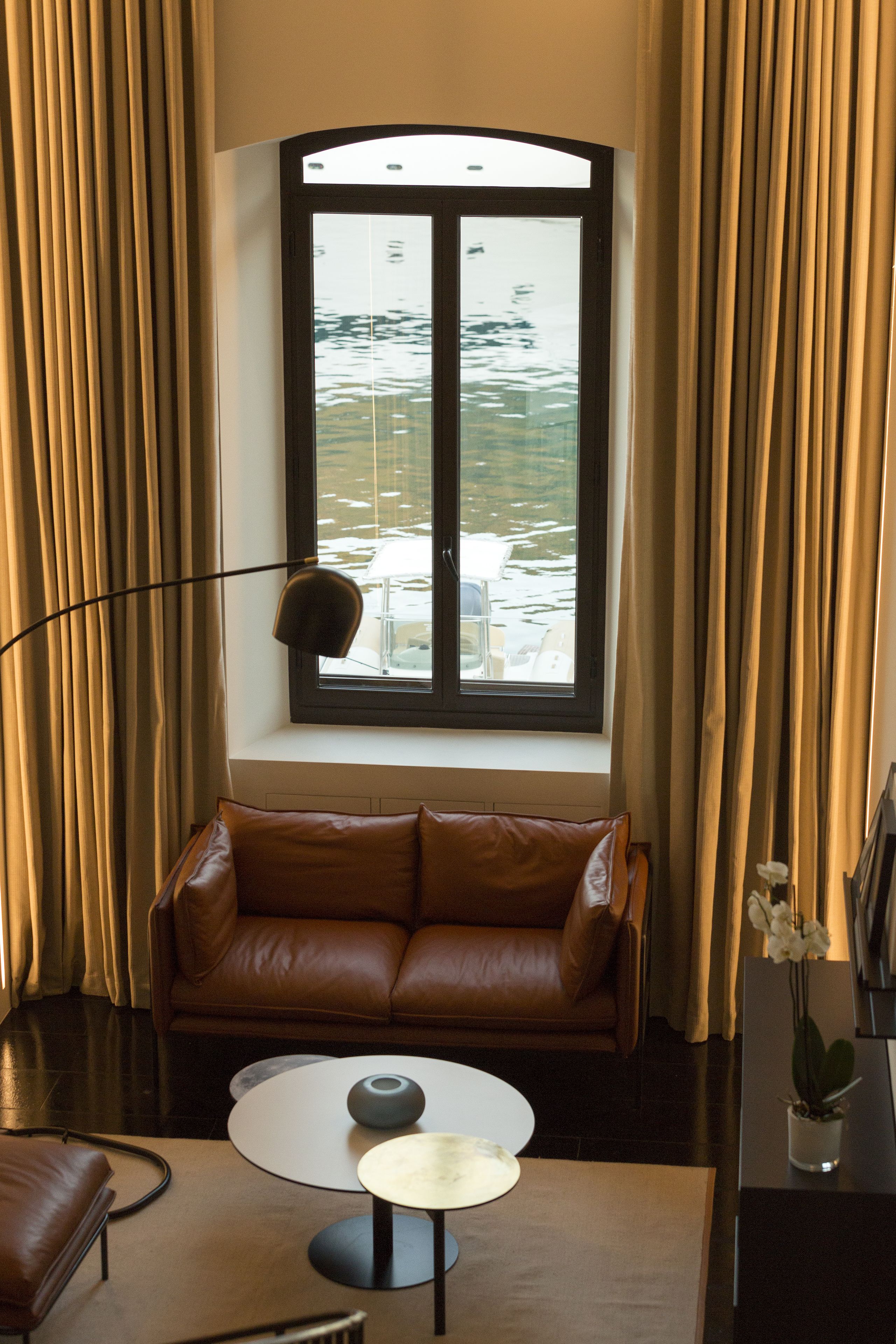 A modern living room with a brown leather sofa, a round coffee table, and a large window with curtains.