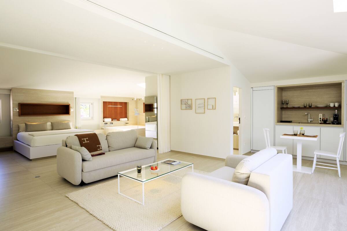 A modern living room with a glass coffee table, two sofas, a kitchen area with white cabinets, and a dining table with chairs.