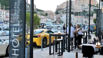 A restaurant with outdoor seating overlooking a marina, featuring a yellow sports car parked nearby.