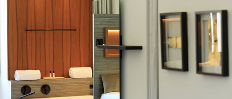 A modern hotel room with a wooden panel wall, a large mirror, a bed with white bedding, and a small bedside table.
