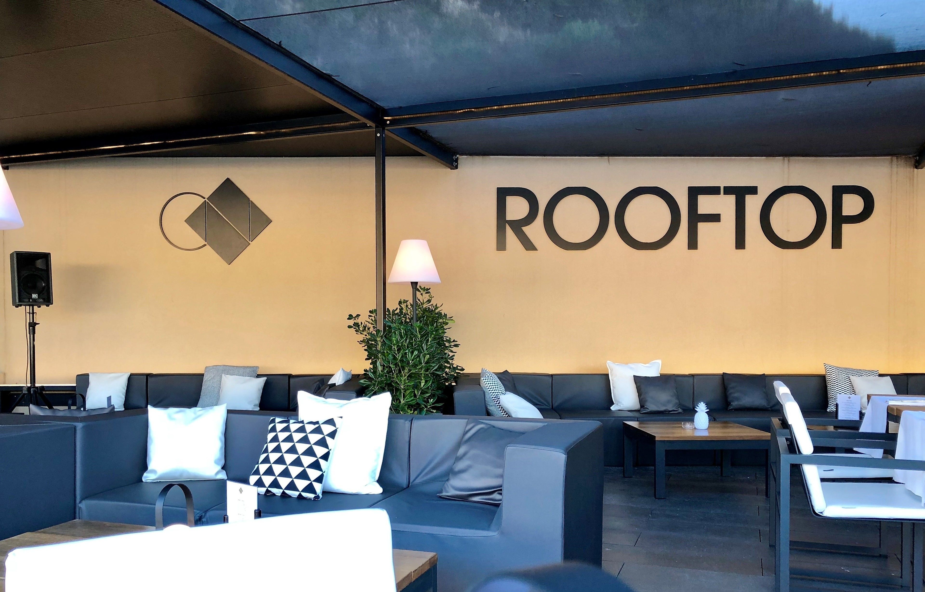 Un área de lounge en la azotea con arreglos de asientos y una pared con el nombre 'ROOFTOP'.