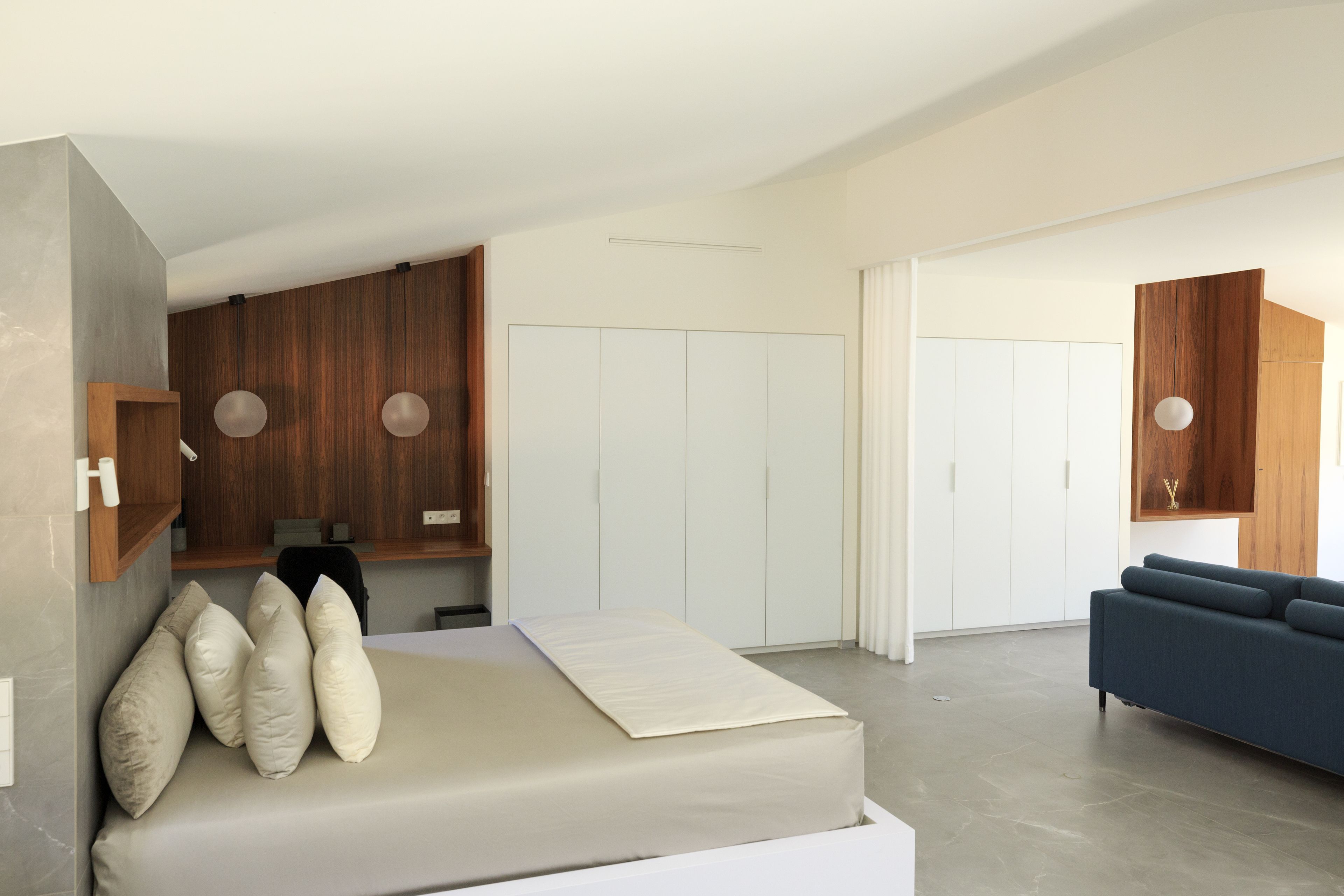 A modern bedroom with a bed, a sofa, wooden panel walls, and a white wardrobe.