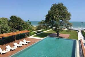 A pool with lounge chairs, a view of the ocean, and a tree. - Baan Thew Talay Blue Sapphire (Cha-am)