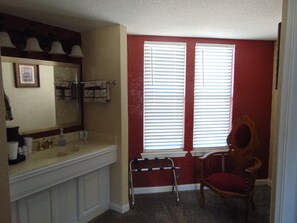 A bathroom with a vanity, a chair, and a window with blinds.