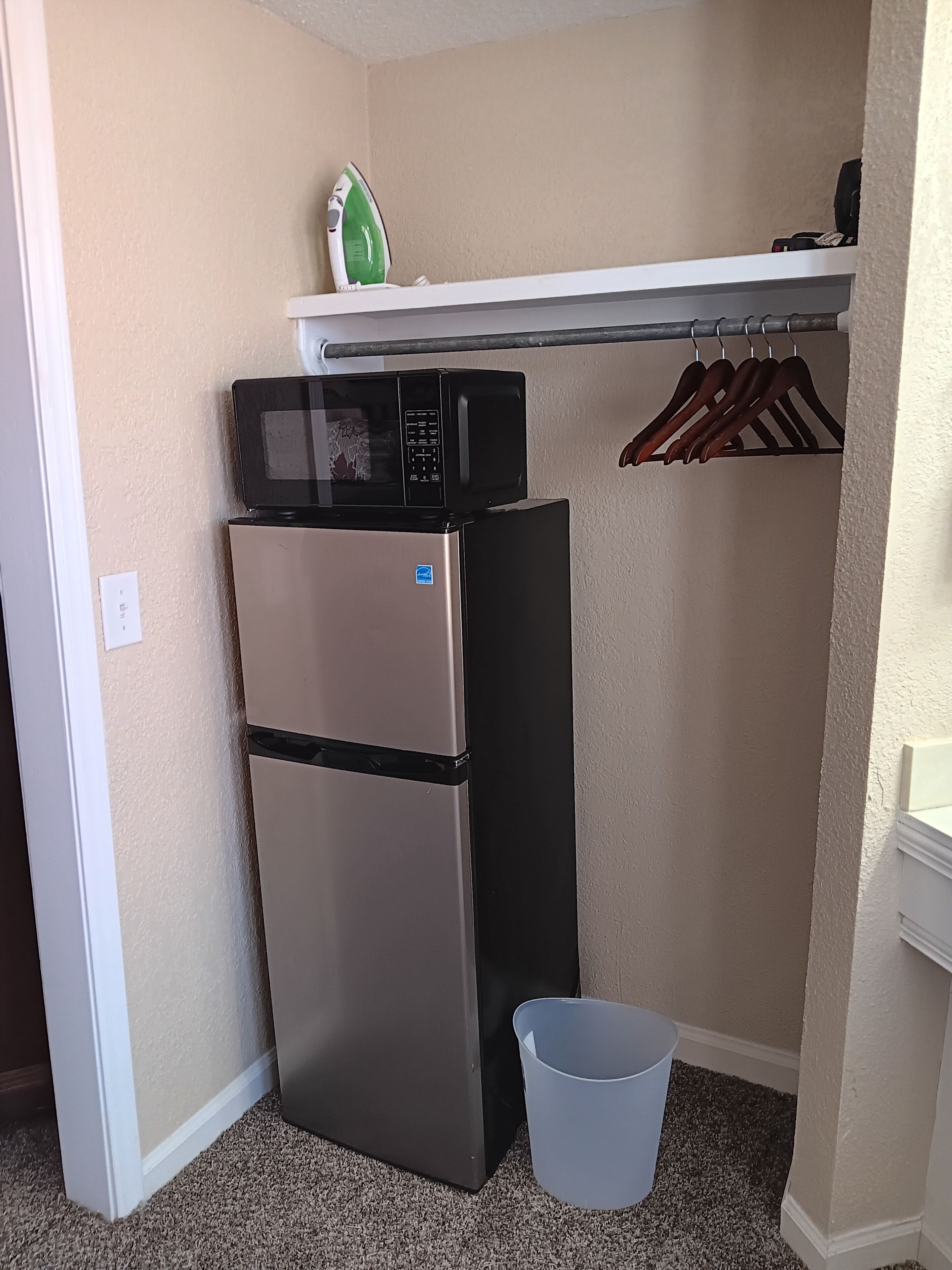 A compact kitchenette with a refrigerator, microwave, and a small shelf above.