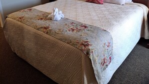 A hotel room with a large bed, a painting on the wall, a nightstand with a lamp, and a floral bedspread.