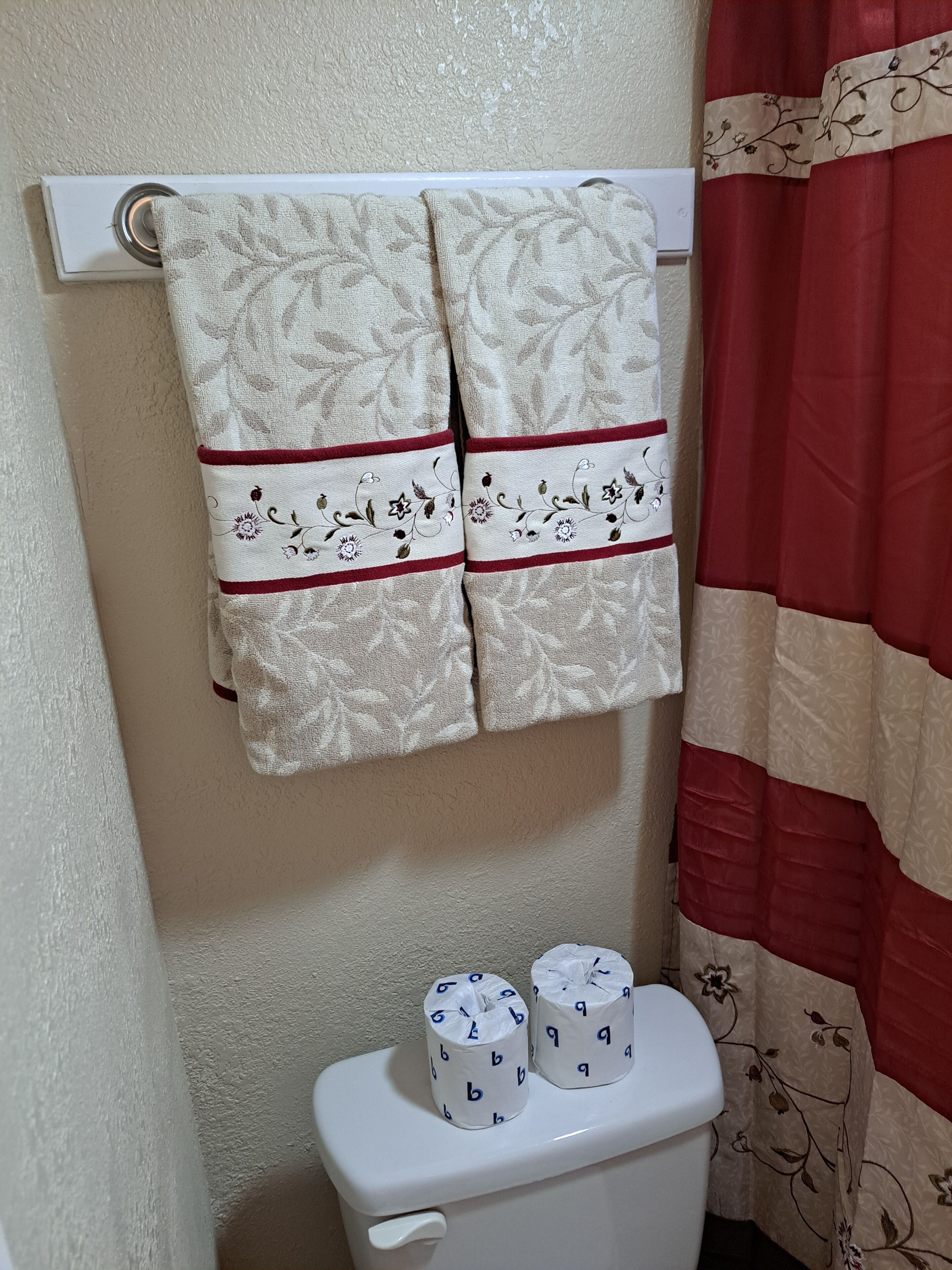 Ein Badezimmer mit Toilette, zwei Toilettenpapierrollen und einem Handtuch an einem Haken.