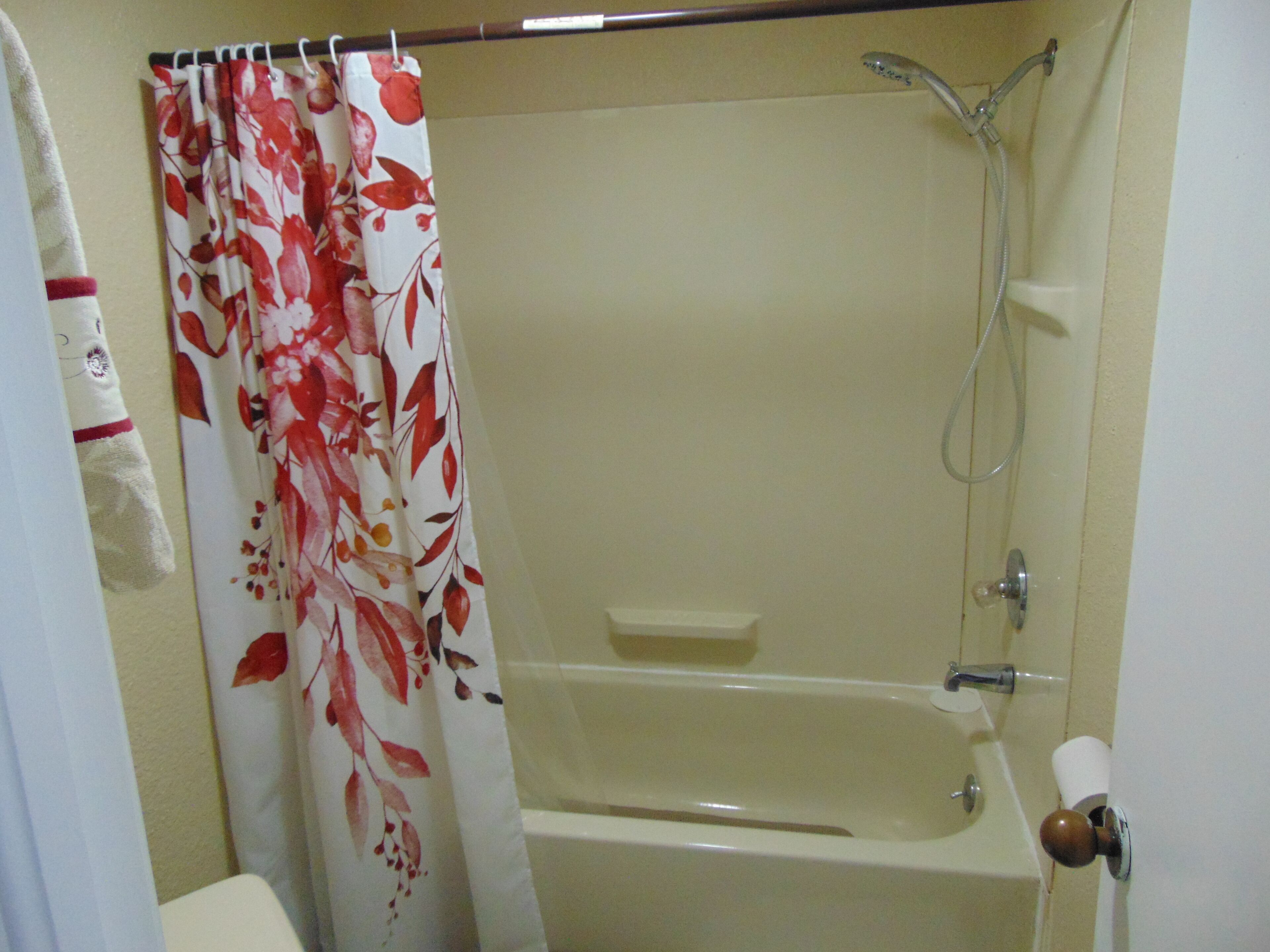 Een badkamer met een badkuip, douche en een gordijn met bloemen.