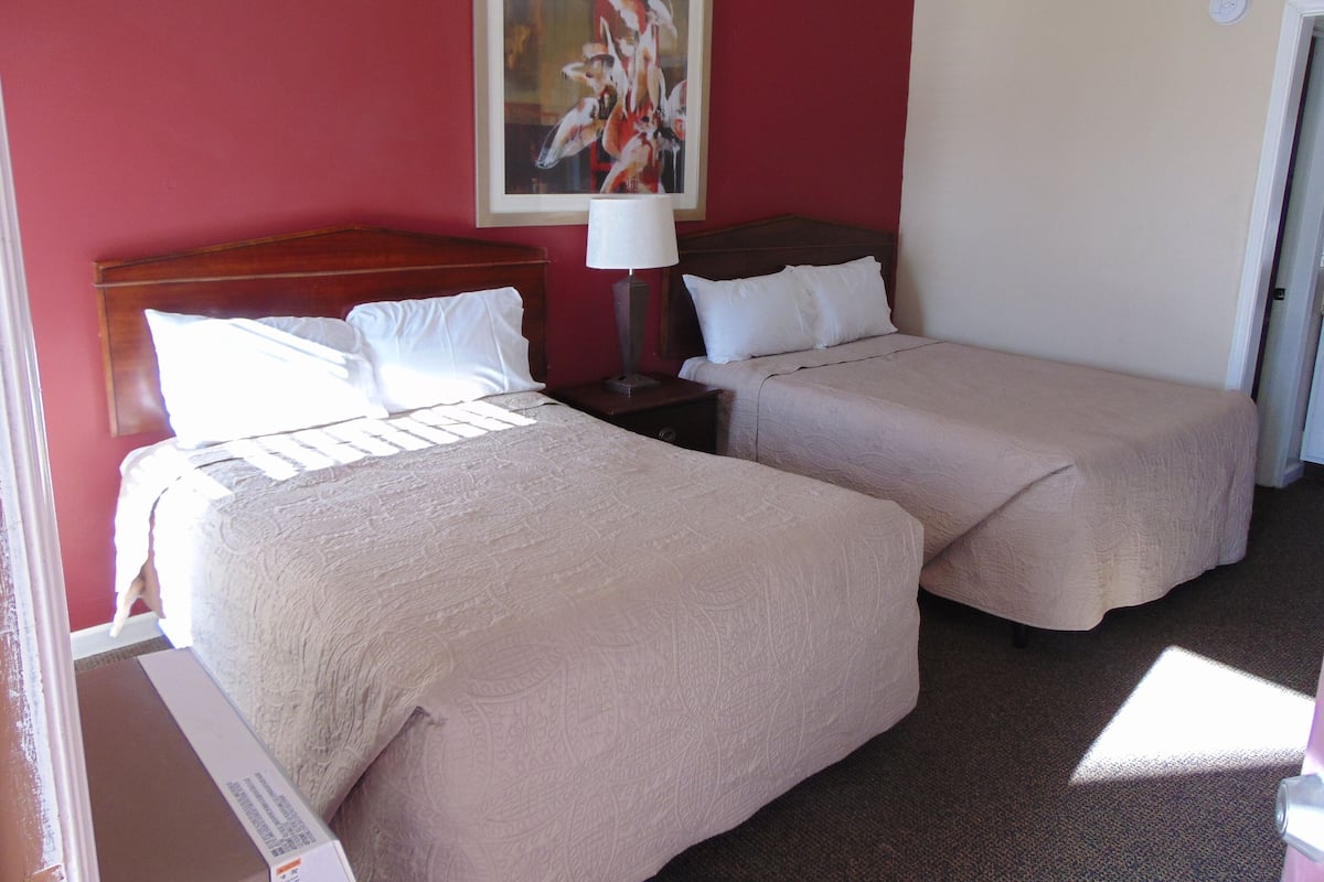A hotel room with two beds, a painting on the wall, and a door.