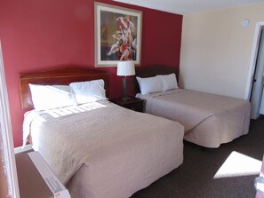 A hotel room with two beds, a painting on the wall, and a door.