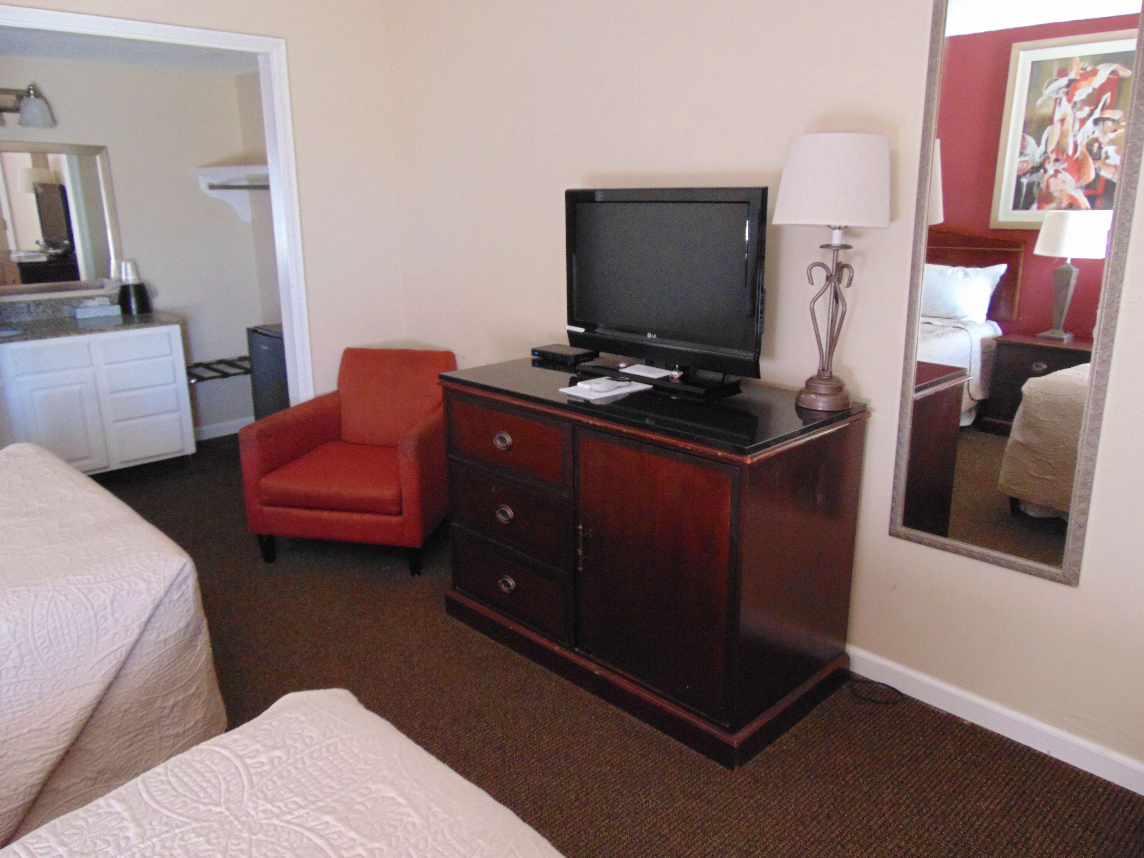 Una habitación de hotel con cama, escritorio con televisor, silla, cómoda y espejo.